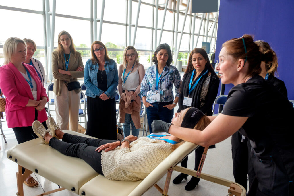 The team from ATA Aesthetic training Academy kick of their hands-on Facial aesthetics workshop around a model who's lying down on a folding demonstration bed.